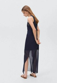 Abito senza maniche di colore navy con pannelli trasparenti nella parte inferiore, fessure laterali e silhouette aderente. Tessuto liscio con una texture morbida, design lungo fino alla caviglia.