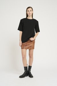 Maglietta nera oversize in cotone, abbinata a una mini gonna in pelle marrone con dettagli di cucitura, e stivali neri alla caviglia con tacco a blocco.