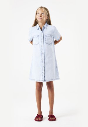 Hellblaues Denim-Hemdkleid mit kurzen Ärmeln, vorderem Knopfverschluss, zwei Brusttaschen und geradem Saum. Getragen mit roten Sandalen.