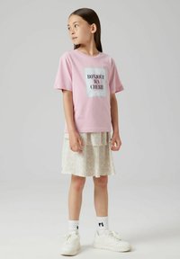 T-shirt di cotone rosa chiaro con "BONJOUR MA CHERIE" stampato in nero su uno sfondo glitterato, abbinato a una gonna a strati con motivo floreale.