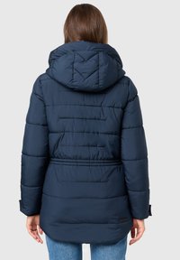 Marineblå pufferjacka med huva, med en quiltad design, elastisk midja och muddade ärmar. Materialet verkar slätt med en mjuk textur.