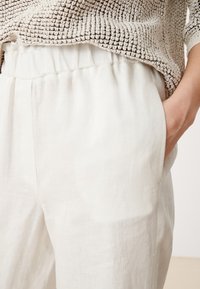 Vita linnbyxor med elastisk midja, avslappnad passform och sidofickor. Ytan är jämn med en subtil glans.