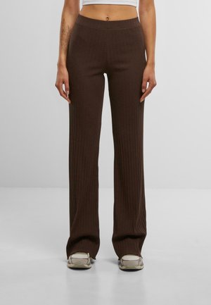 Pantalons marron côtelés avec une taille élastique, des jambes évasées et une texture douce. Associés à des baskets de couleur claire.