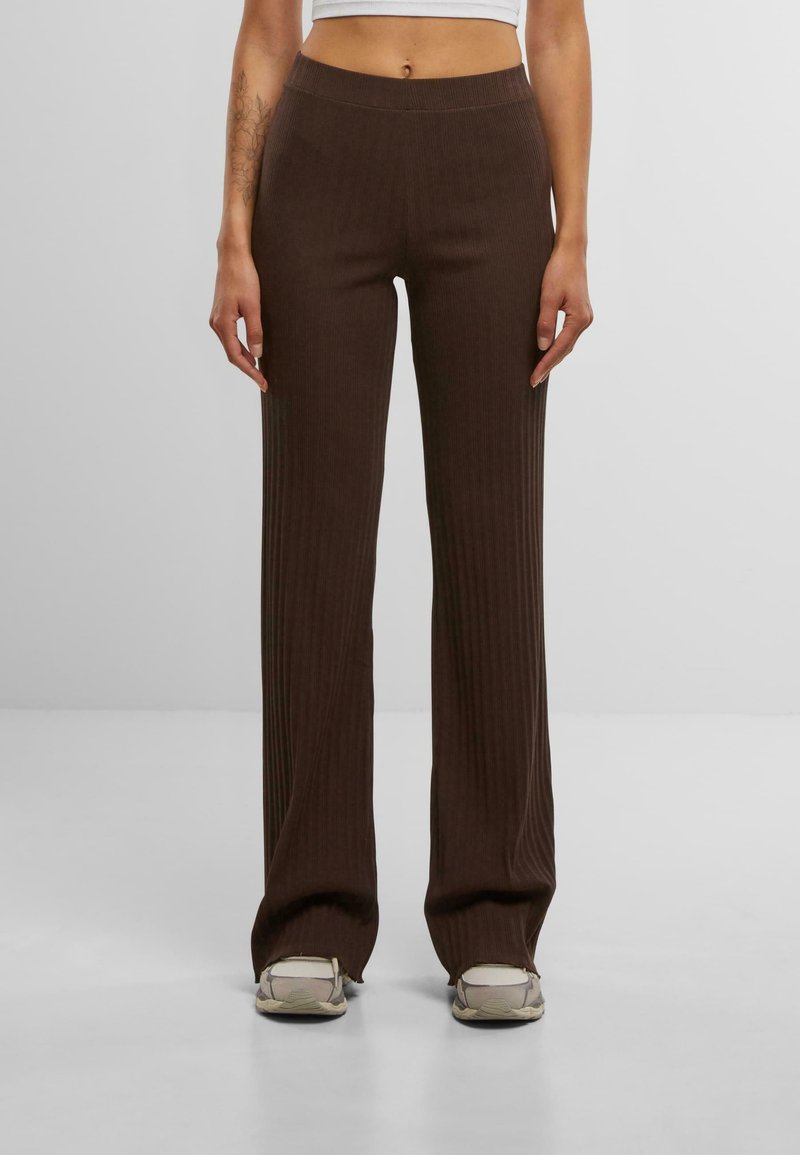 Pantalons marron côtelés avec une taille élastique, des jambes évasées et une texture douce. Associés à des baskets de couleur claire.