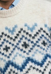 Pull en tricot avec une base crème et un motif géométrique bleu et noir, col rond et texture douce.