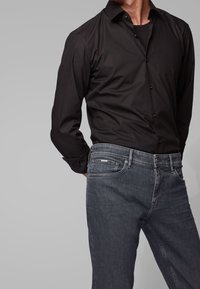 Black button-up shirt with a smooth texture, worn with dark denim jeans featuring a slight fade and five-pocket design.