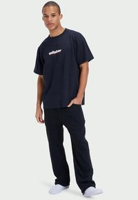 Marineblå bomulds T-shirt med rund halsudskæring og korte ærmer, prydet med et rødt og hvidt "Quiksilver" logo på forsiden. Kombineret med sorte bukser.