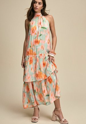 Abito lungo floreale in verde pastello con motivi arancioni e rosa, caratterizzato da un collo a halter, livelli sovrapposti e una silhouette fluida.