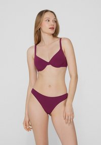 Zestaw bikini w głębokim burgundzie, z usztywnianym biustonoszem z regulowanymi ramiączkami oraz bezszwowymi, niskimi majtkami. Gładka tekstura i minimalistyczny design.