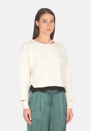 Maglione bianco a coste con dettagli in pizzo sul bordo, dotato di scollo rotondo e maniche lunghe, abbinato a pantaloni in satin verdi.