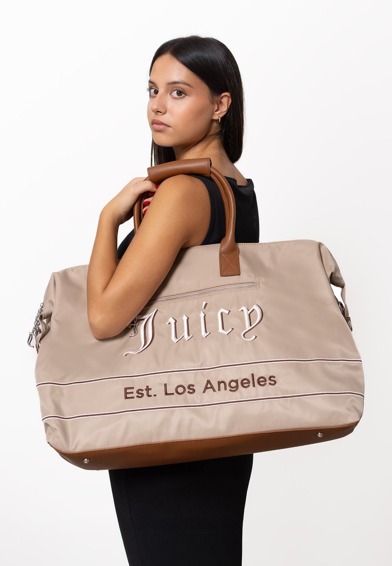 Borsa da viaggio in nylon beige con dettagli in pelle marrone. Presenta il logo ricamato "Juicy" e "Est. Los Angeles" con strisce orizzontali.