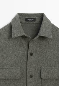Grå filtet skjorte med krave, der har to brystlommer, fire sorte knapper og en mærkat med teksten "Massimo Dutti".