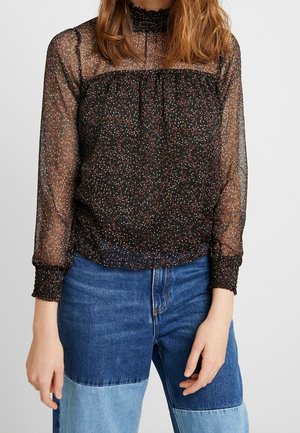 Blouse noire transparente avec un col à volants et des manches longues, présentant un motif de pois multicolores dispersés et des poignets élastiqués.