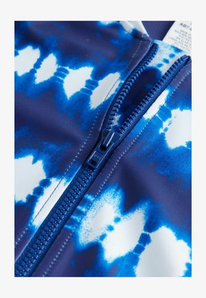 Mėlynas ir baltas rash guard'as su marškinėlių dažymo raštu, viduriniu mėlynu užtrauktuku ir sklandžia, tampria audinio tekstūra.