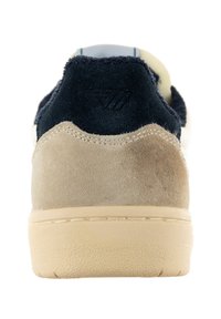 Scarpa sportiva in suede con una combinazione di colori beige e blu navy, caratterizzata da un tallone texturizzato e una suola in gomma color crema. Accenti di design semplici.