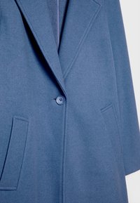 Tmavě modrý kabát s výřezovým límcem, zapínáním na jeden knoflík a bočními kapsami; vyrobený z texturované, měkké látky.