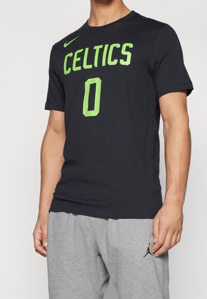 Mann trägt ein schwarzes Celtics Basketball-T-Shirt mit neongrünem Text und graue Jogginghose mit schwarzem Logo am linken Oberschenkel.