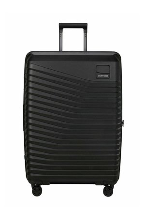 Valise rigide noire avec motifs en vagues horizontales, quatre roulettes, poignée extensible et logo Samsonite en haut à droite.