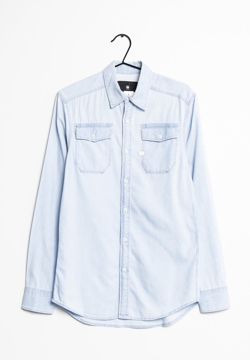 Light blue denim shirt with long sleeves, button-up front, two chest pockets, and a rounded hem. Features a standard collar and white buttons.