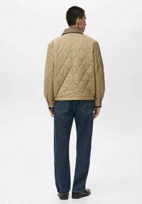 Giacca marrone trapuntata con colletto nero, dallo stile a lunghezza completa, indossata con jeans in denim blu, vista da dietro.