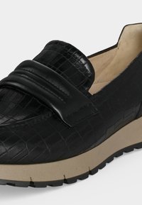 Mocassin noir avec motif crocodile texturé, bride en cuir lisse, semelle beige rembourrée et semelle extérieure en caoutchouc crantée.