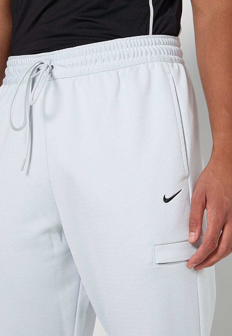 Lichtgrijze sportbroek met elastische tailleband, trekkoord, gestructureerde stof, zijzak en zwart Nike-logo op de dij.