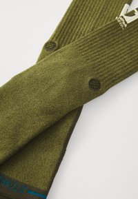 Green knit socks with a ribbed texture, featuring black logo accents and a blue line near the cuff. Soft, regular fit, casual design.