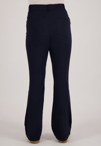 Marineblauwe broek met achterzakken, elastische tailleband en licht uitlopende pijpen, gedragen door een persoon die staat op een lichte achtergrond.