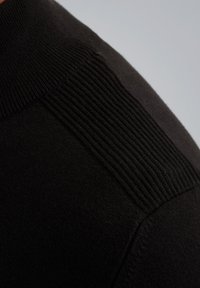Vêtement tricoté noir avec une texture lisse et des accents côtelés sur les épaules. Le design met l'accent sur une silhouette ajustée.