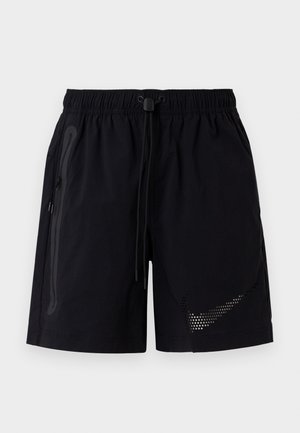 Mustad treeningpüksid, millel on elastne vöökoht, reguleeritav pael, lukuga küljetasku ja täpiline Nike logoga paremal eesmisel säärel.