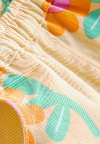 Gros plan sur un tissu beige avec un imprimé floral orange et vert et un détail de couture élastique sur un vêtement.