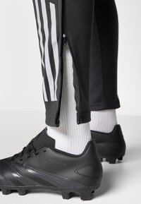 Black athletic pants with zipper detail and white stripes, paired with black soccer cleats and white ribbed socks.