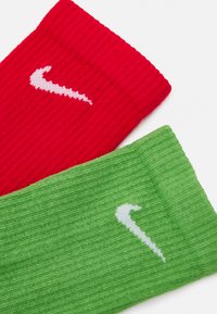 Czerwone i zielone skarpetki dzianinowe z ryżowym splotem. Każda ma białe logo Nike Swoosh na mankiecie.