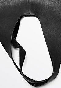 Sac en cuir noir avec un design découpé unique et une texture lisse. Comprend une seule sangle large pour le porter.