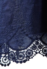 Námorně modrá látka s propracovanou květinovou výšivkou a detailním krajkovým lemem s kruhovými vzory a vlnitými okraji.