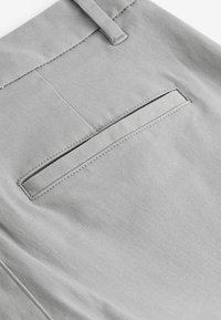 Pantalonii din țesătură gri au un buzunar plat pe spate, cu cusături curate și o textură netedă. Materialul pare a fi durabil și ușor.