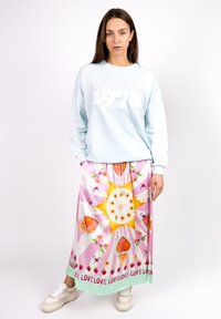 Hellblaues Sweatshirt mit "California 1978" in strukturiertem Weiß. Maxirock mit floralem Muster in Pink, Gelb und Grün, kombiniert mit beigen Sneakers.