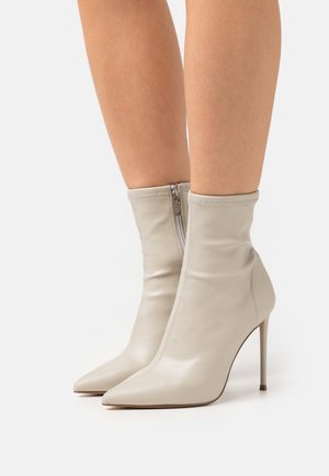 Bottines à bout pointu en cuir beige clair avec un design ajusté, dotées d'une fermeture éclair sur le côté et de talons aiguilles hauts. Texture lisse dans l'ensemble.