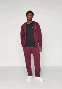 Karmīnu krāsas kapuce ar priekšējām kabatām, saskaņota ar melnu T-kreklu un karmīnu krāsas sporta biksēm ar logo. Baltas kedas, vienkāršs dizains, mīksts audums.