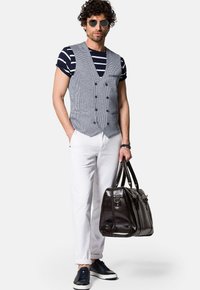 Szary kamizelka w wzór houndstooth, granatowa i biała koszulka w paski, białe spodnie, czarne sneakersy oraz ciemnobrązowa skórzana torba z krótkimi uchwytami.