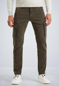 Pantalons cargo vert olive fabriqués en tissu durable, avec plusieurs poches zippées et une coupe fuselée. Portés avec des baskets blanches.