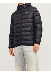 Sort dunjakke med hætte, med vandrette syninger, lynlåslukning foran, sidelommer og elastiske ærmer. Båret over lyseblå jeans.