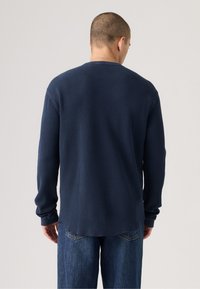 Marineblauwe longsleeve shirt met een textuur en ribbelontwerp. Beschikt over een ronde halslijn en een relaxte pasvorm. De stof voelt zacht aan en heeft opgerolde mouwen.