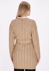 Beige pletený kardigan s texturovaným vzorem, s páskem v pase a dlouhými rukávy. Obsahuje vertikální žebrování a jednoduchý design límce.