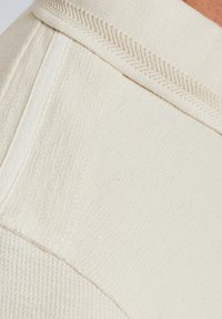 Tissu en tricot crème clair avec un motif texturé, présentant un col côtelé et des détails de couture subtils le long des bords.
