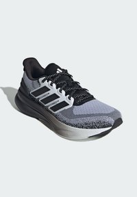 Chaussure de course grise et noire avec une tige en maille, semelle épaisse, rayures blanches et lacets noirs. Texture lisse avec des détails texturés.