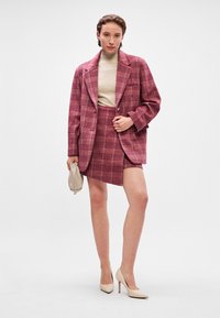 Textured burgundy plaid blazer paired with a matching mini skirt, complemented by a beige turtleneck and nude high heels.