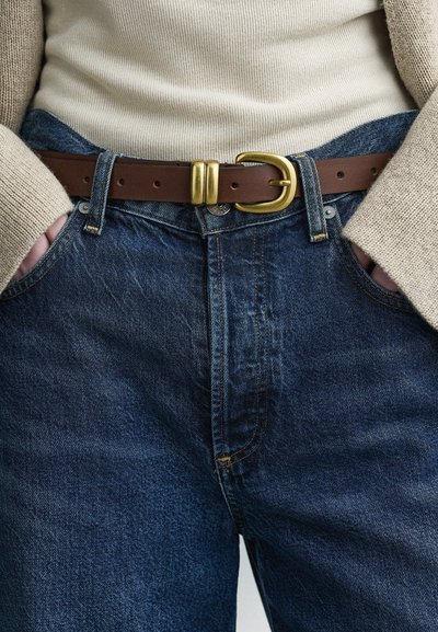 Μπλε τζιν παντελόνι με χαλαρή εφαρμογή, με καφέ δερμάτινη ζώνη με χρυσή αγκράφα, εμφανείς ραφές και δύο μπροστινές τσέπες.