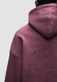 Felpa con cappuccio viola caratterizzata da un materiale testurizzato, un dettaglio del logo ricamato distintivo e un design con vestibilità rilassata e maniche ampie.