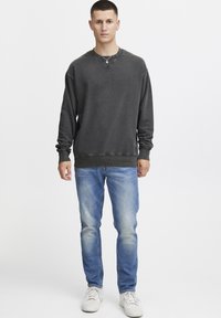 Sweat-shirt gris foncé à col rond et manches côtelées, associé à un jean bleu clair et des baskets blanches. Design d'ensemble simple et décontracté.